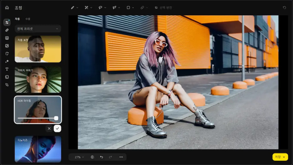 모바일 AI 사진 편집 자동화로 손쉽게 완성하는 스마트 사진 관리 4 보라색 머리와 흰색 선글라스를 쓴 사람이 회색 셔츠와 부츠를 착용하고 주황색 방지턱 옆에 앉아 있다. 배경에는 주황색과 검은색 패턴의 현대적인 건물이 보인다.